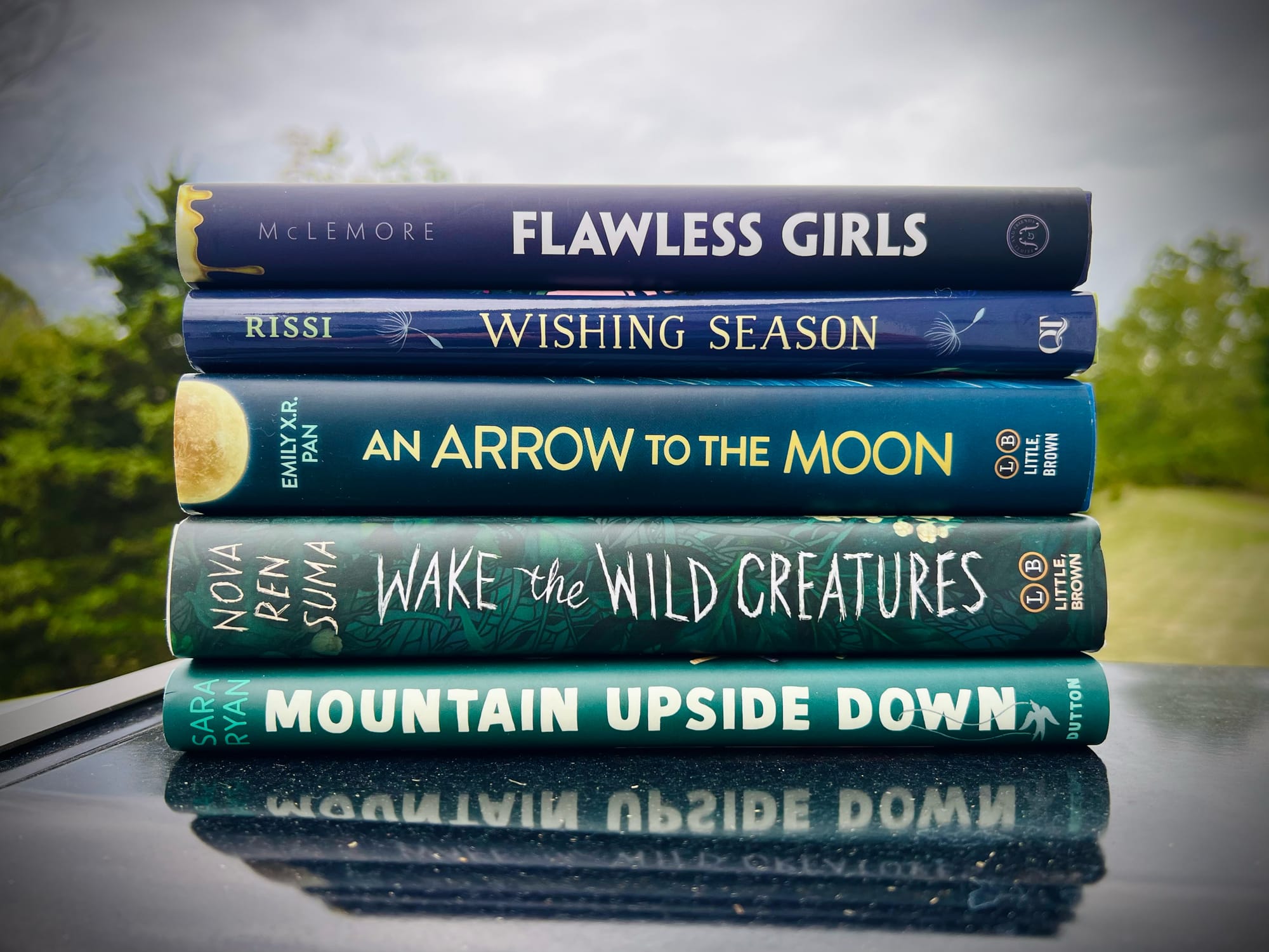 A stack of books consisting of one title from each author: Flawless Girls by Anna-Marie McLemore, Wishing Season by Anica Mrose Rissi, An Arrow to the Moon by Emily X.R. Pan, Wake the Wild Creatures by Nova Ren Suma, Mountain Upside Down by Sara Ryan