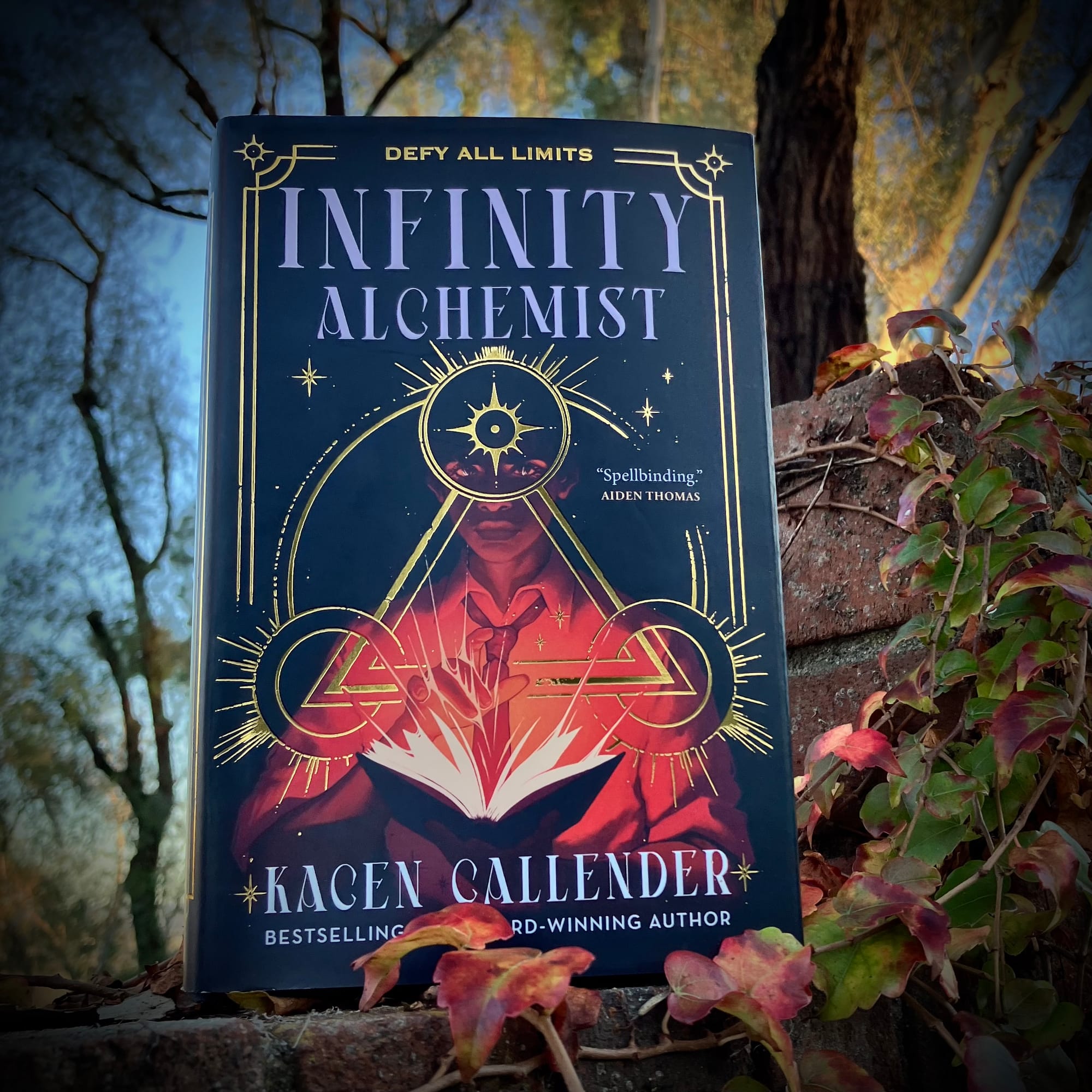 Hardcover of Kacen Callender’s INFINITY ALCHEMIST on top of an ivy-covered brick wall.  