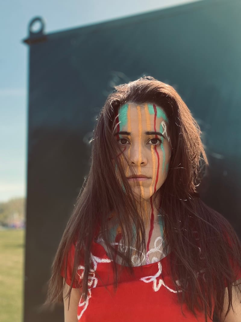 Second image is framed slightly closer in than the first, and A-M’s hair is blowing into their face.